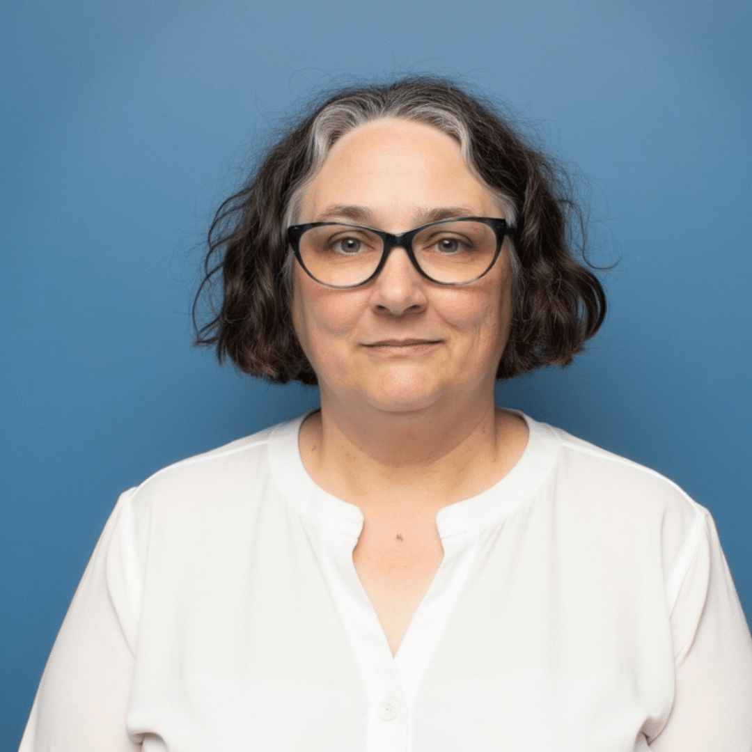 Robin Elise Weiss smiles in a white shirt on a blue background in her headshot.